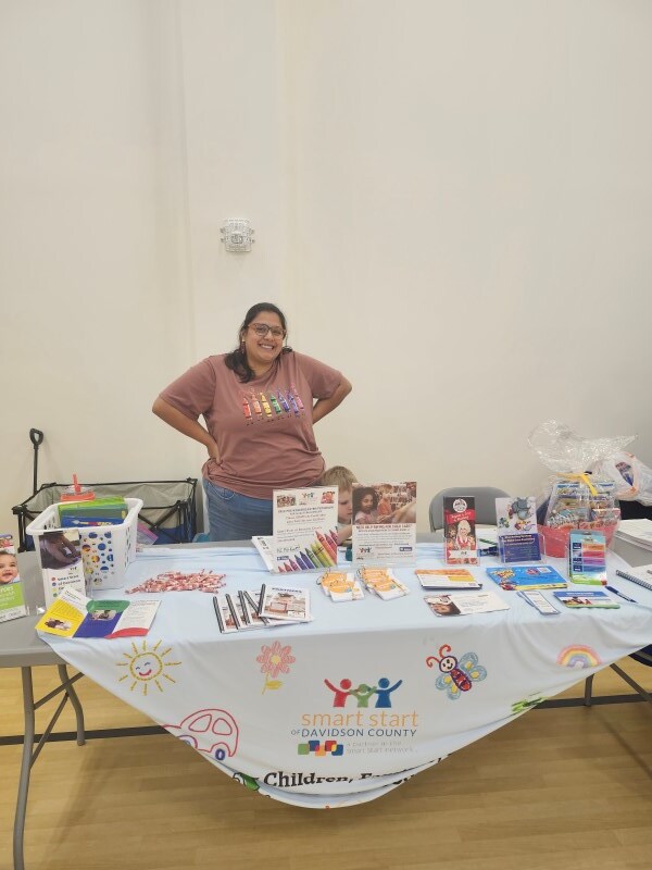 A woman standing behind a table.